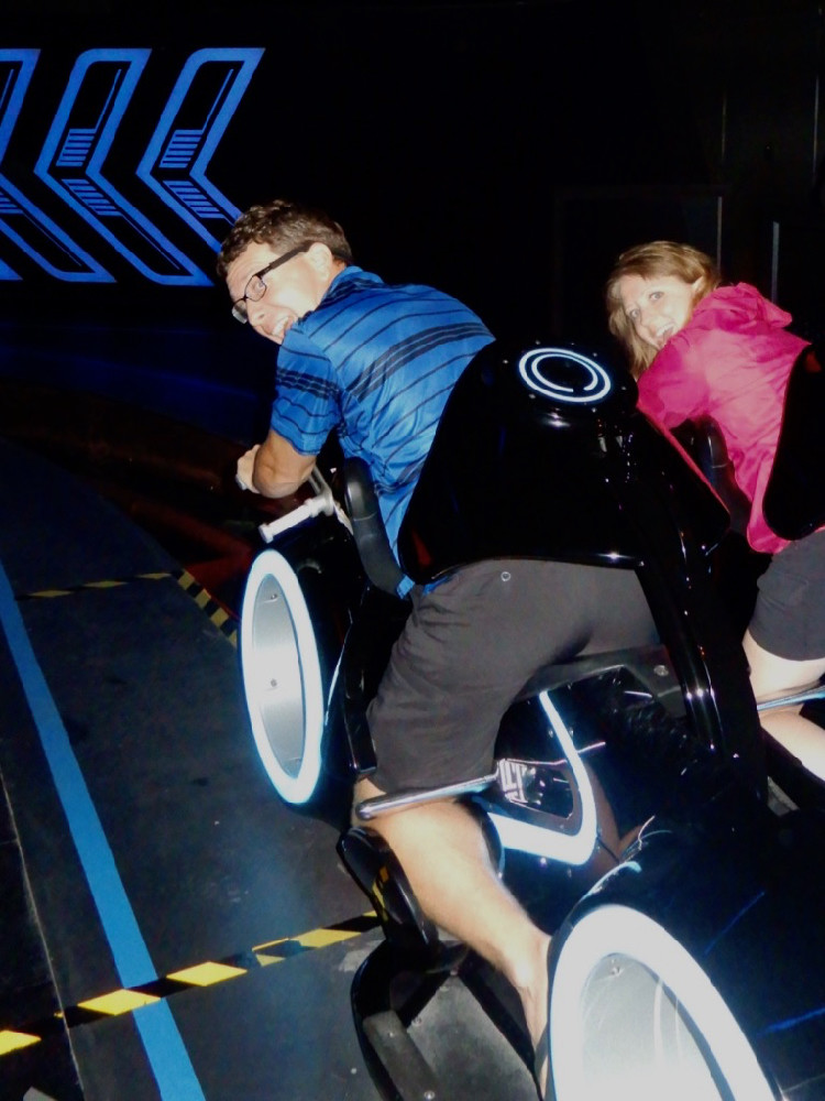 a man and woman sit on the Tron Lightcycle Power Run ride vehicles in Shanghai Disneyland park