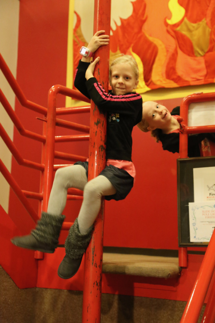 an elementary school girl slides down a fire pole at the Cincinnati Fire Museum - a great staycation idea in Cincinnati